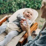 Joyful Laughing Baby Holds Finger Of Mother’s Hand.